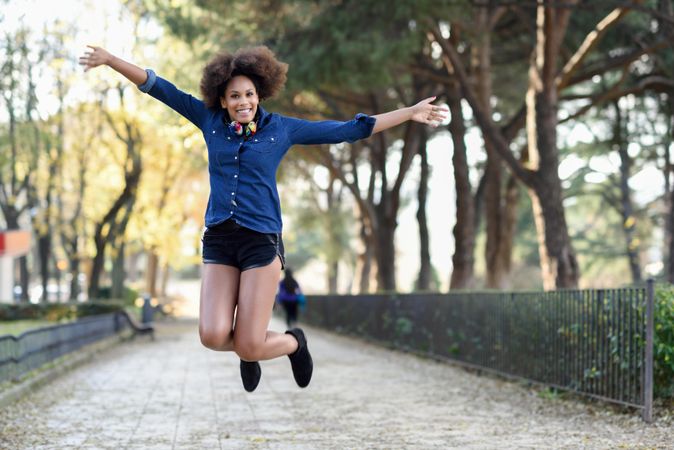 Female jumping in denim shirt with open arms in front of trees