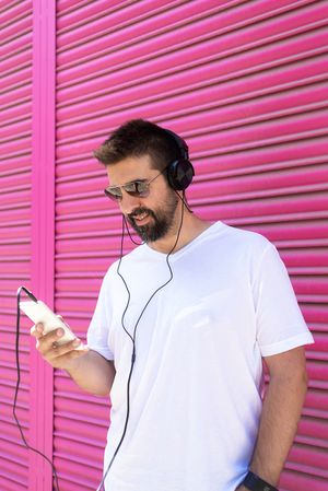 Man in headphones checking phone in front of pink wall