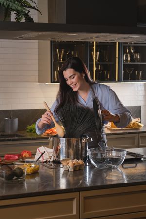 Happy female chef cooking squid ink spaghetti in kitchen