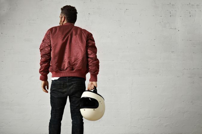 Rearshot of man in dark red leather jacket holding helmet in hand