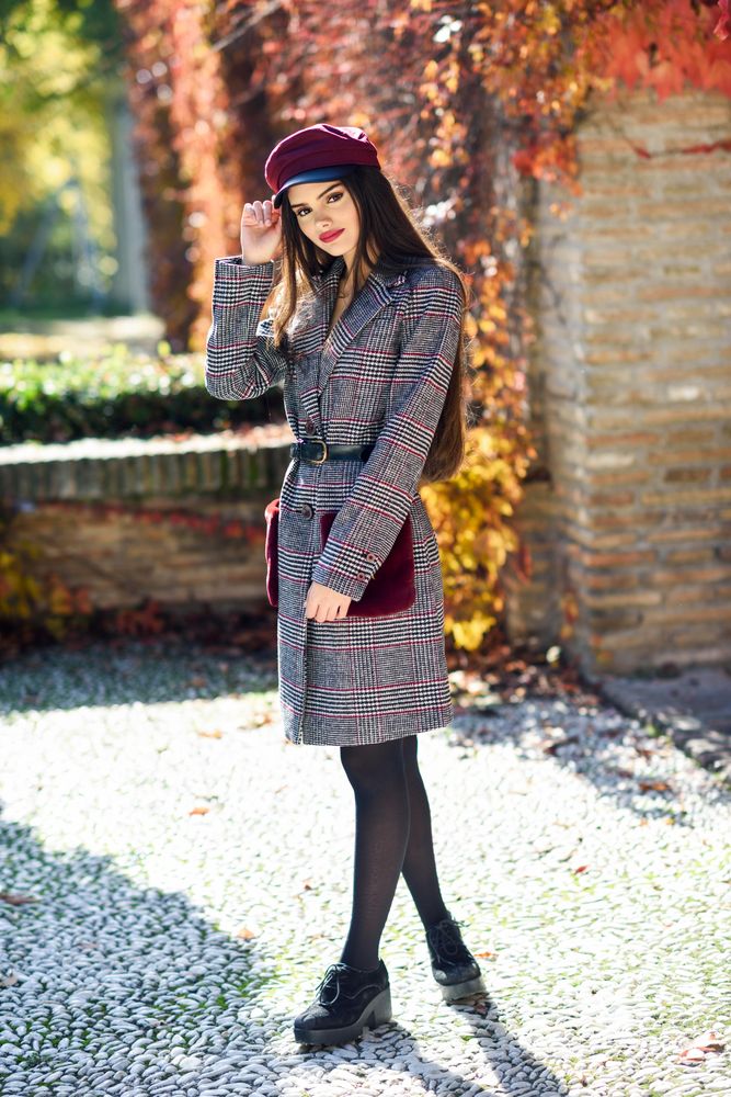 Shy female in warm winter clothes standing outside on sunny day holding her hat