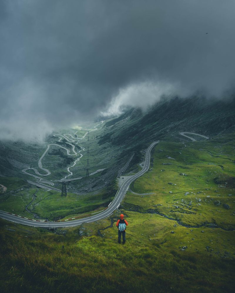 Person with backpack walking on green grass near Transfăgărășean road  in Romania