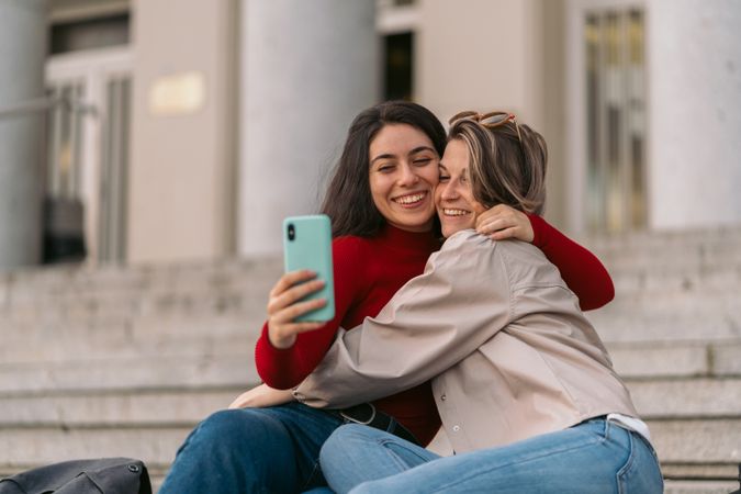 two students smiling taking a selfie sitting on the stairs of the college.