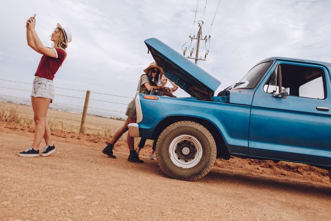 Female friends examining broken down car on country road