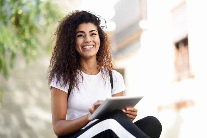 Smiling Arab woman with her digital tablet sitting outdoors