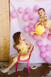 Kids having fun with watering can against wall with balloons