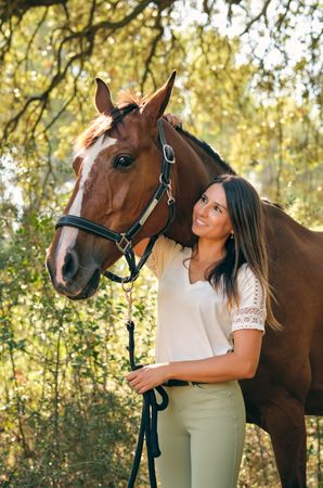 Young woman stroking horse in forest
