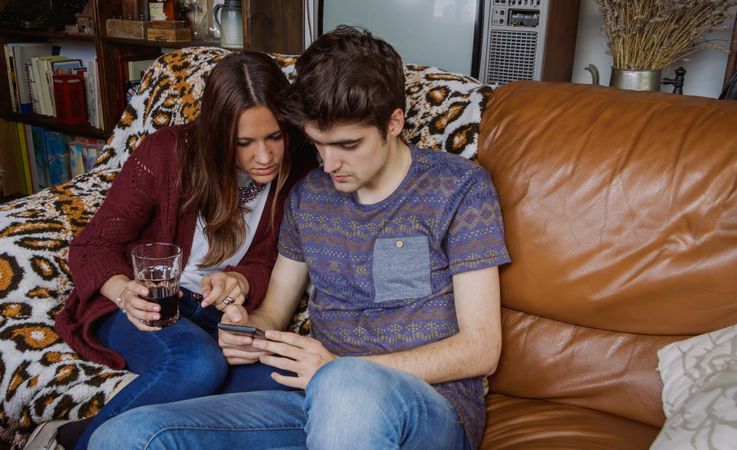 Young couple looking smartphone sitting on sofa