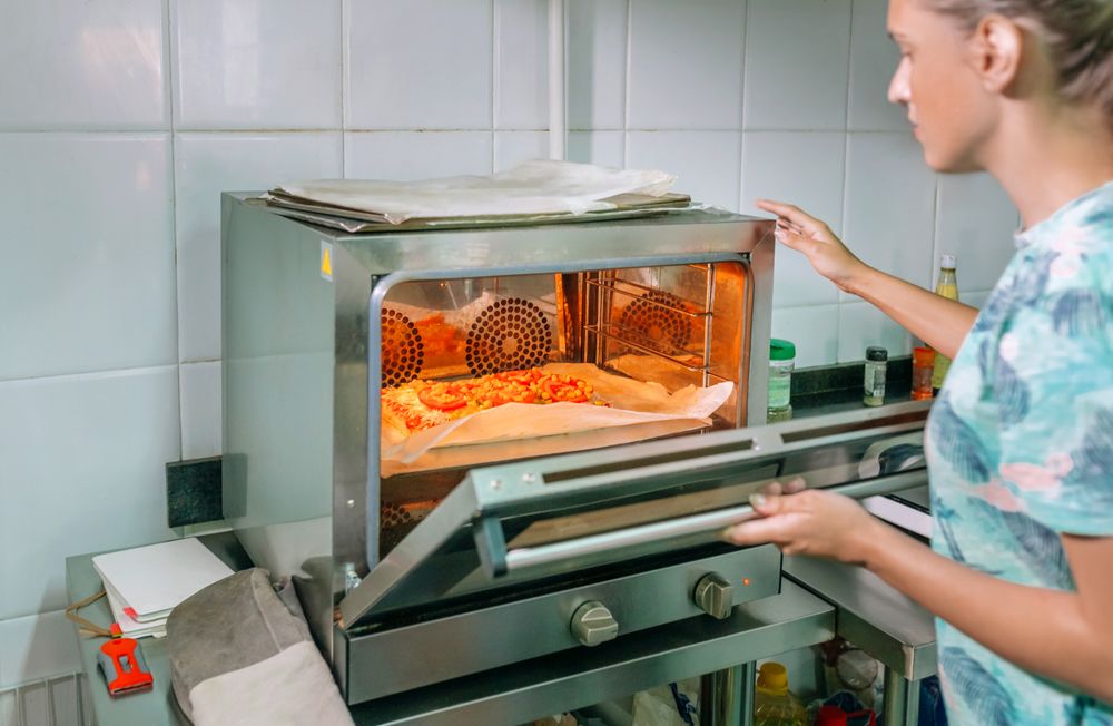 Unrecognizable professional cook opening oven door to take a pizza out in a restaurant kitchen