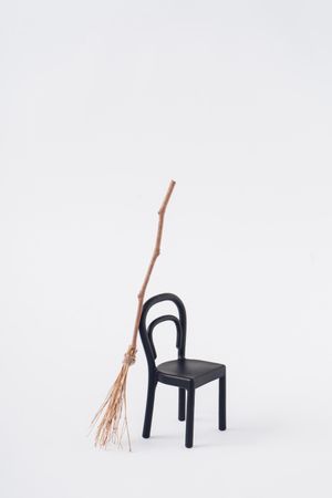 Broomstick leaning on chair on light  background