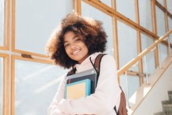 Teenage female student standing on stairs in school holding text books