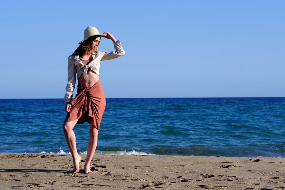 A fashion model with a hat at the beach before sunset