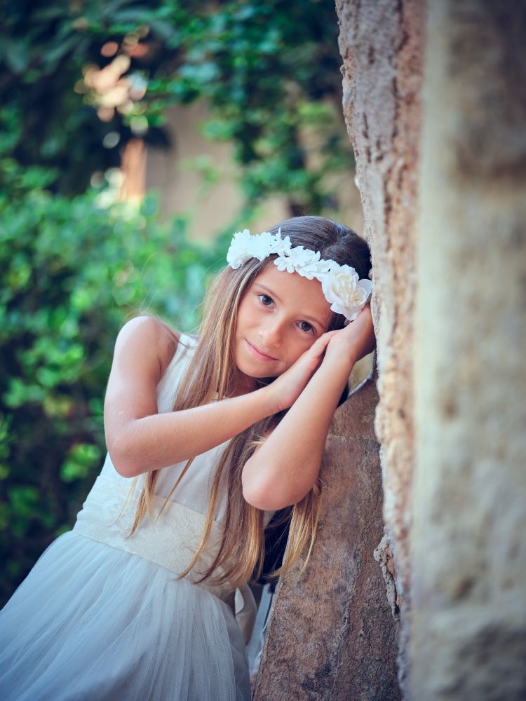 Young woman in bridal dress leaning on wall while looking at cam