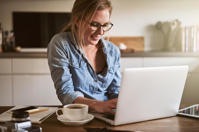 Woman smiling at laptop with a cup of coffee