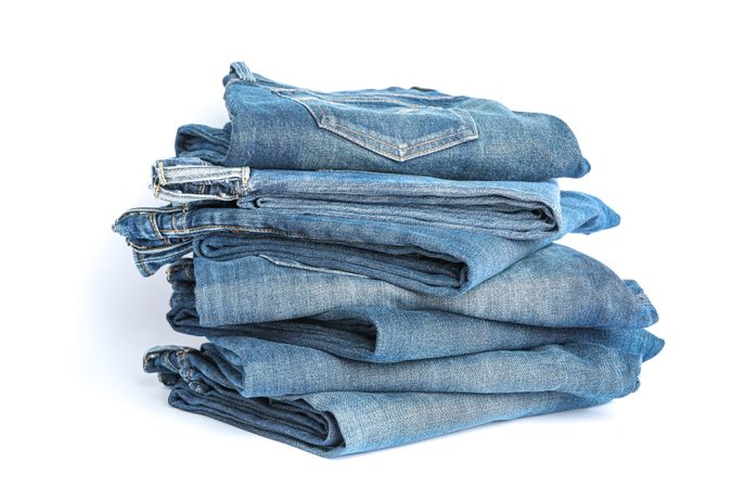 Stack of blue jeans on light background, space for text