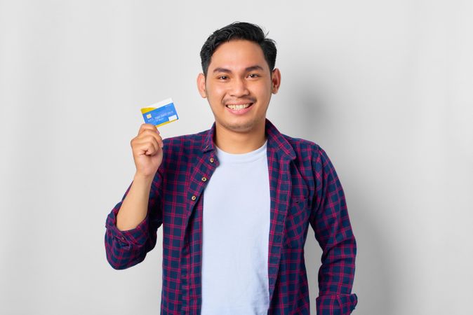 Happy Asian male in grey studio with credit card held up