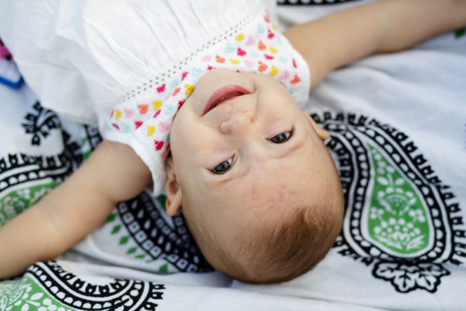 Joyful charming baby lying on blanket and looking at camera