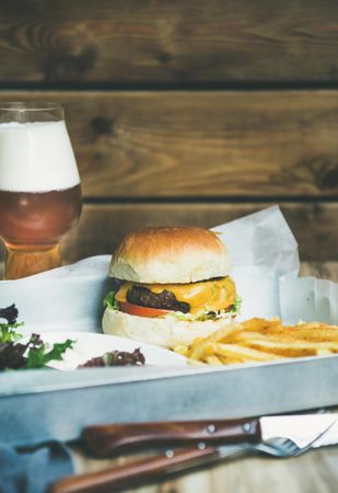 Classic hamburger with fries and beer at wooden restaurant table
