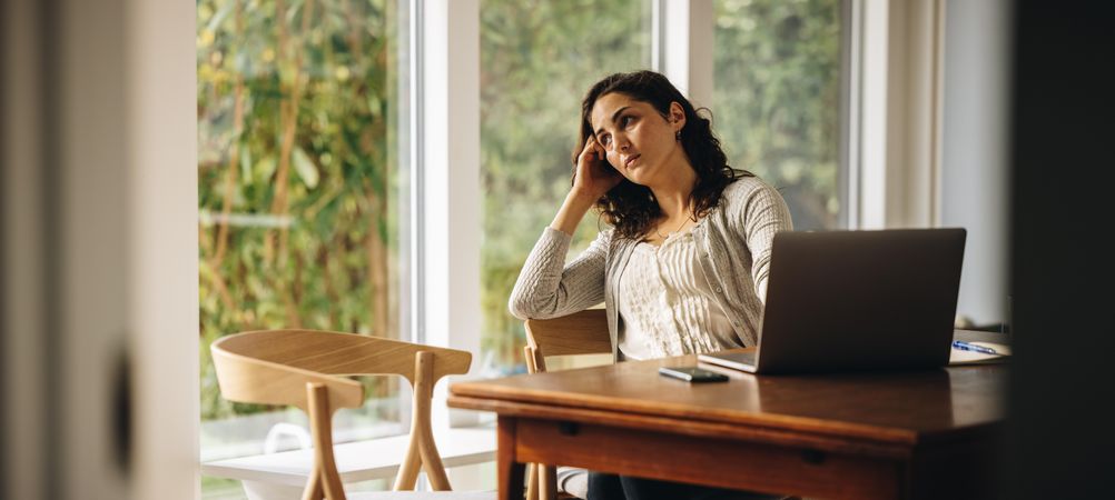 Woman lost in deep thought while working on laptop