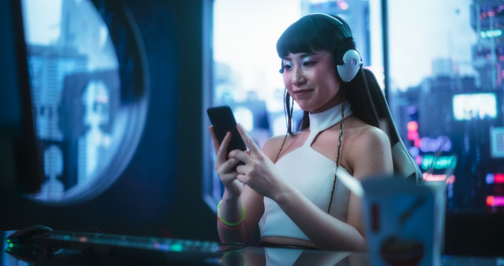 Smiling Asian Female Using Smartphone while Sitting Behind a Desk in a Futuristic Cyberpunk Office Space.