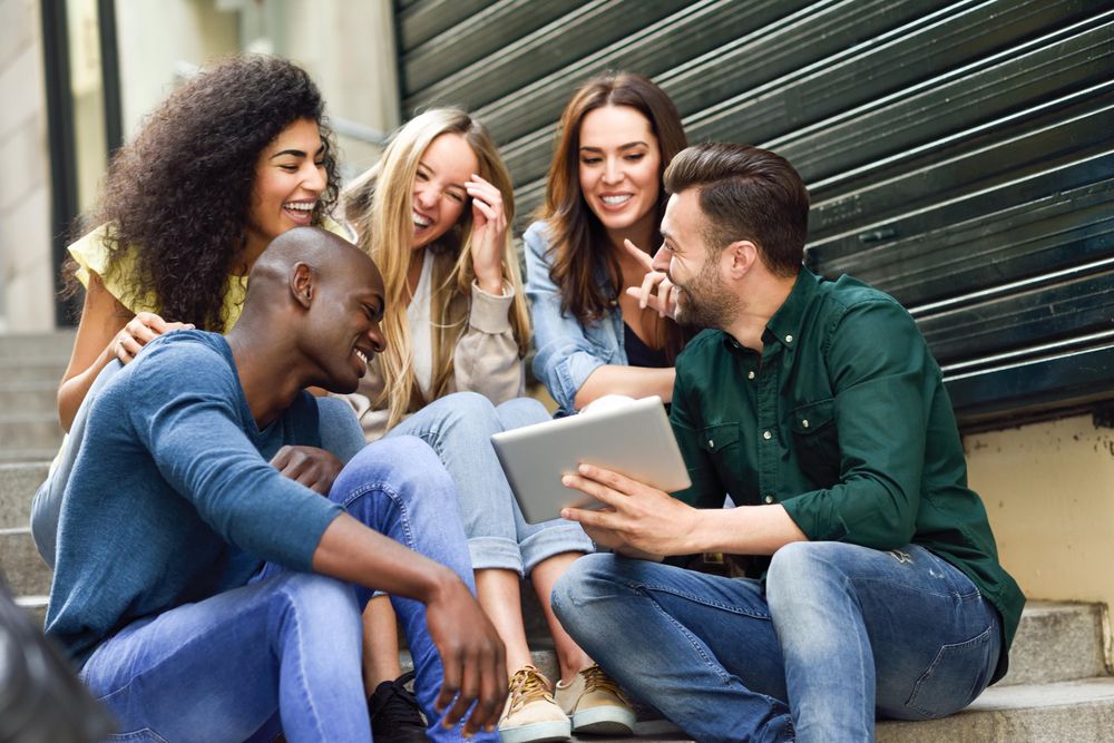 Friends laughing at something on digital tablet while sitting on outdoor cement staircase