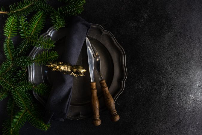 Top view of dark plate with knife and fork with pine branch