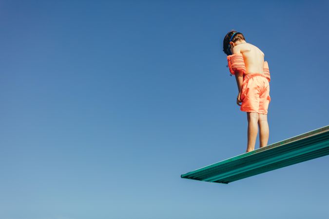 Boy standing on diving spring board against blue sky