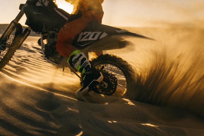 Motocross rider driving bike through sand dune
