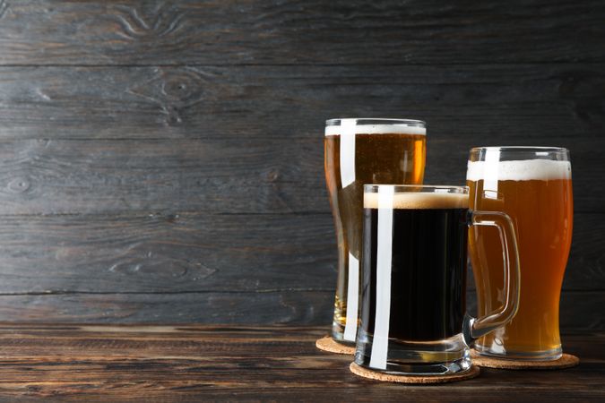Different mugs with beer on wooden table, copy space