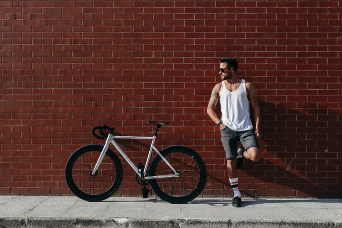 Sportive man standing next to brick wall with bike