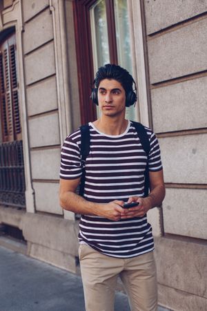 Young man with headphones and smartphone walking outdoors