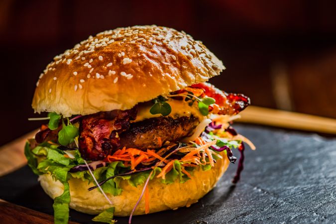 Double hamburger with meat, cheese and different vegetables on dark rustic background with copy space