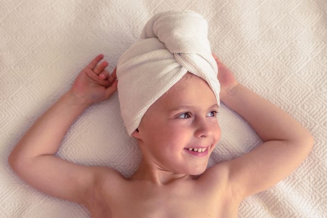 Smiling kid with towel on head on bed
