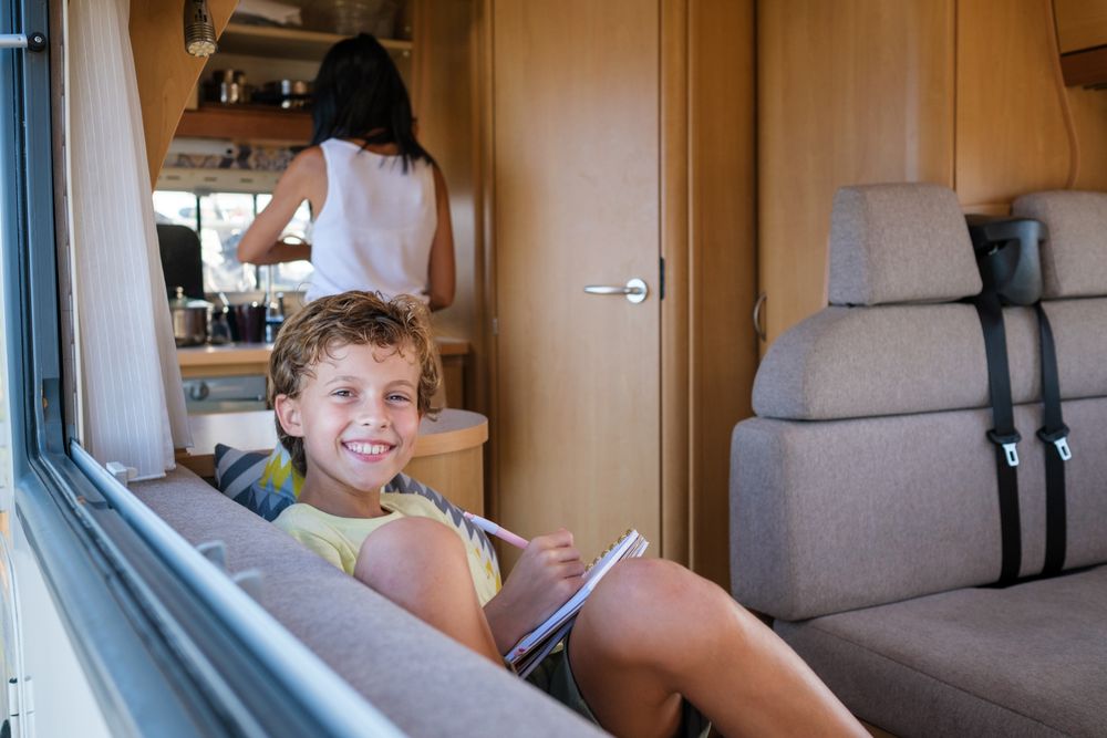Delighted boy writing in diary near camper window