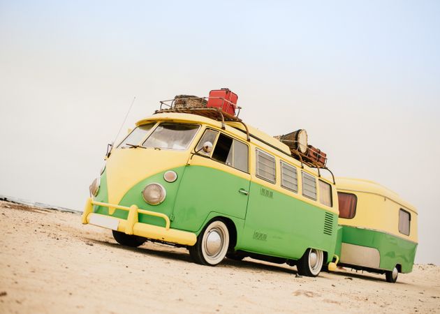 Colorful minibus with trailer parked on sandy shore in sunny day