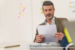 Grey haired businessman with  beard, sitting at desk, reading a document 5qkDOw