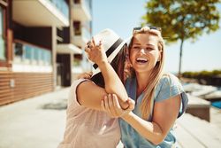 Two female friends laughing and walking along the river on a sunny day