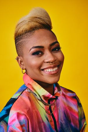 Content Black woman in bright 80s windbreaker jacket in yellow studio