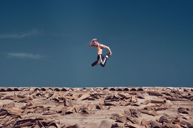 Strong active man jumping on roof while performing freestyle dance