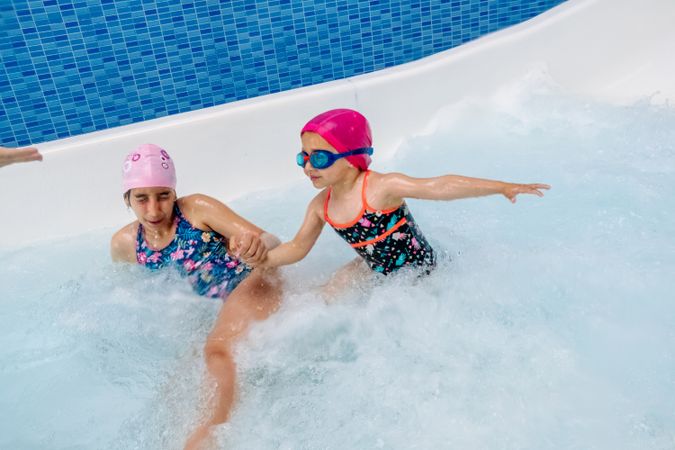 Cheerful girls in hat smiling and swimming in pool in water park