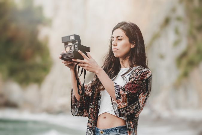 Woman with camera on shore near stones and water