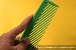 Hand holding green hair comb diagonally against yellow background 49m9Wn