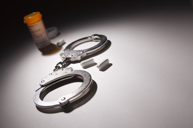 Handcuffs, Medicine Bottle and Pills Under Spot Light