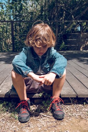 Sad preteen boy sitting on wooden boardwalk