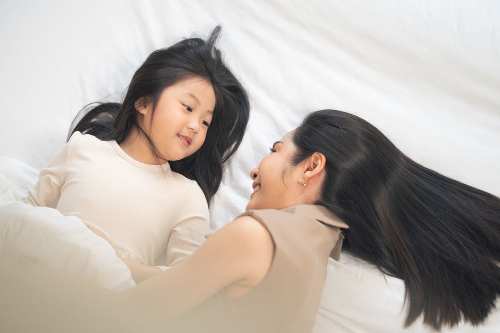 Top view of Asian mother and daughter cuddle and talking on bed.