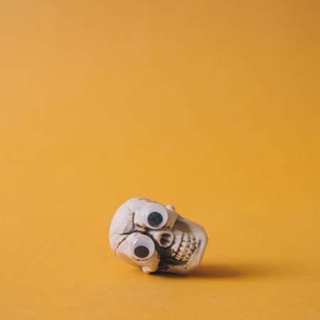 Halloween skeleton head with googly eyes and orange background lying on its side