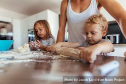 Little boy with his mother and sister preparing dough with rolling pin on kitchen table 4jEw95