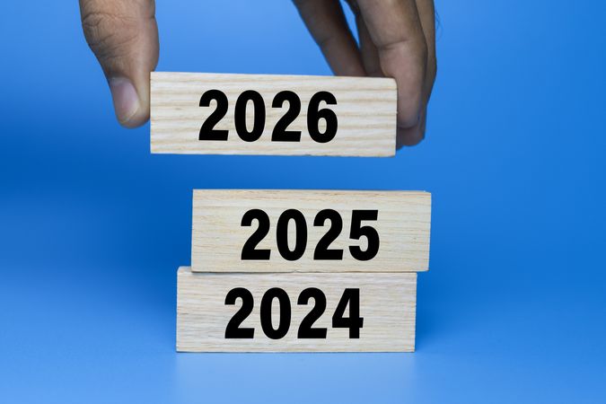 male hand put wooden blocks with year 2024, 2025, and 2026 isolated on blue background