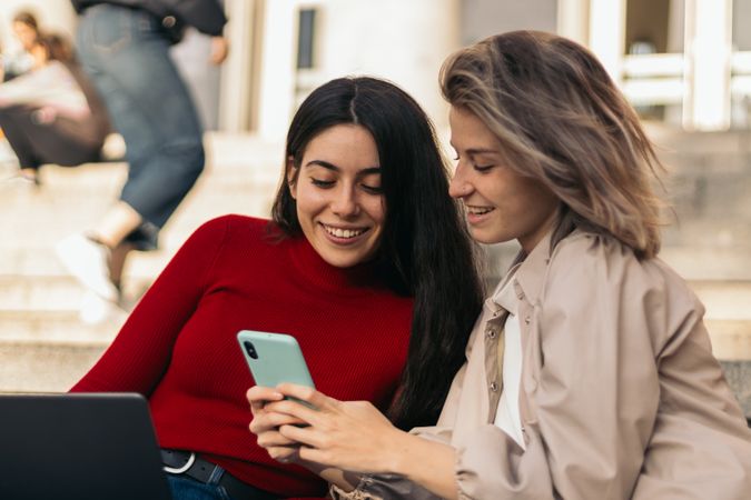 Two students sitting on the stairs of the college with the laptop and the mobile. Close-up
