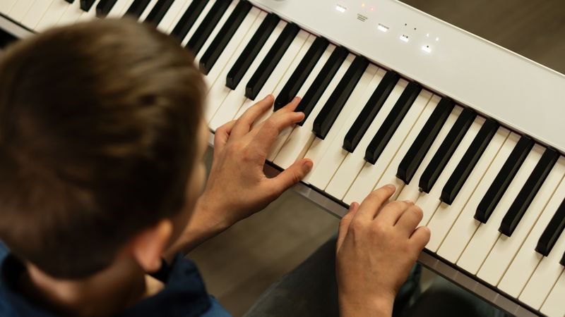 Boy playing white digital piano indoors, focusing on keys.